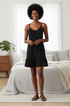 A black sleeveless camisole-style dress with thin shoulder straps, a gathered neckline, and a ruffled hem, shown flat against a light beige background.