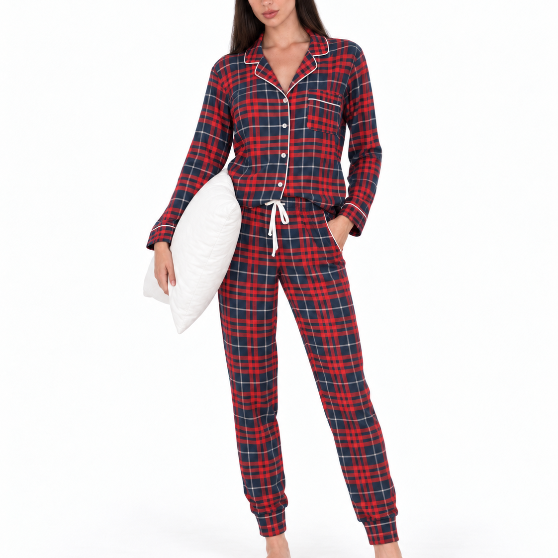 A woman modeling a red and navy plaid pajama set with white piping, holding a white pillow against a plain white background.