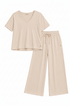 A two-piece loungewear set in a light cream-beige color, featuring a short-sleeve V-neck top and matching wide-leg drawstring pants, laid flat on a solid beige background.