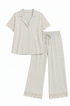 A light gray two-piece pajama set featuring a short-sleeve button-front top with lace sleeve panels and matching wide-leg pants with lace hem trim, displayed on a solid beige background.