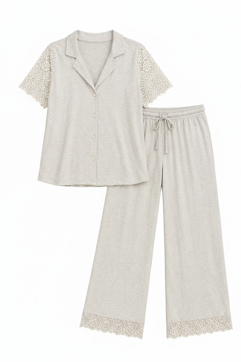 A light gray two-piece pajama set featuring a short-sleeve button-front top with lace sleeve panels and matching wide-leg pants with lace hem trim, displayed on a solid beige background.