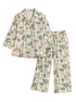 A two-piece pajama set featuring a long-sleeve button-up shirt and matching wide-leg pants, both printed with a tropical palm tree and palm leaf pattern in shades of green and beige on an off-white background.